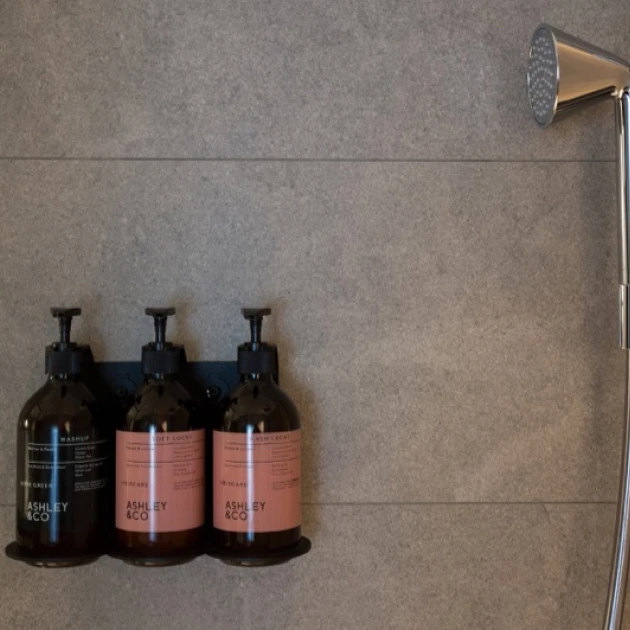 partners-ashleyco-1 three bottles of toiletries on a shower shelf