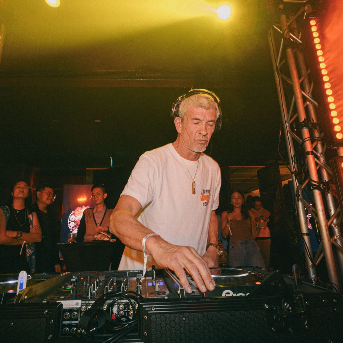 male dj in a club with a small crowd behind him