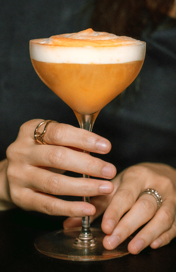 Artboard 1 person holding an orange coloured drink in a glass cup
